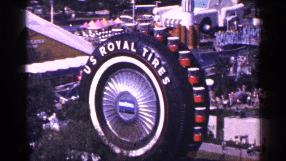 1964 New York home-movie frame focused on the oversized U.S. Royal Tires display with people and exhibits around it.