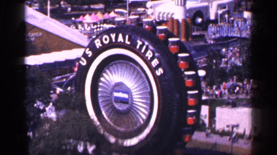 1964 New York frame of the large U.S. Royal Tires exhibit, filmed from above with fairgoers and structures nearby.