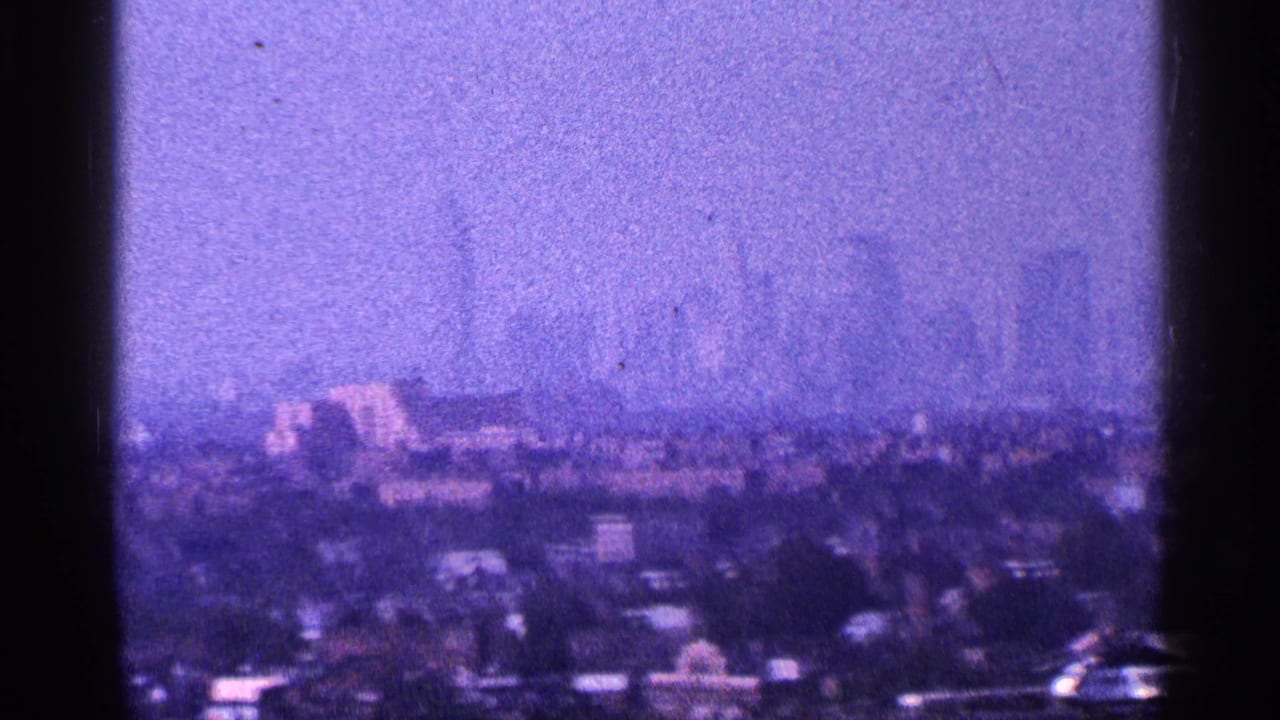 1964 New York City skyline appears in purple-tinted 8mm footage, with low foreground buildings and dark framing at the edges.