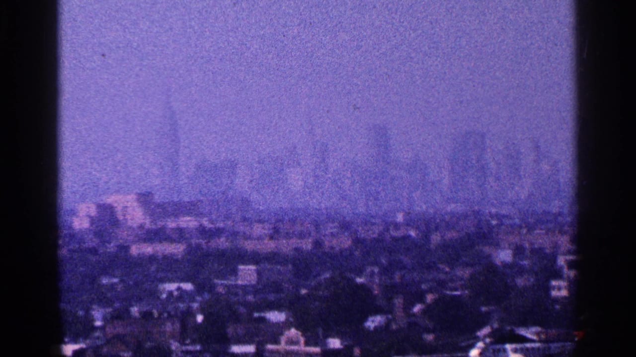 Purple-tinted 8mm frame of the New York City skyline, with high-rise silhouettes softened by haze beyond lower buildings.