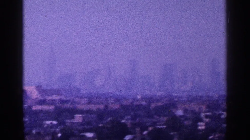A hazy 1964 New York City panorama in purple-tinted 8mm, with skyline forms barely visible above foreground structures.