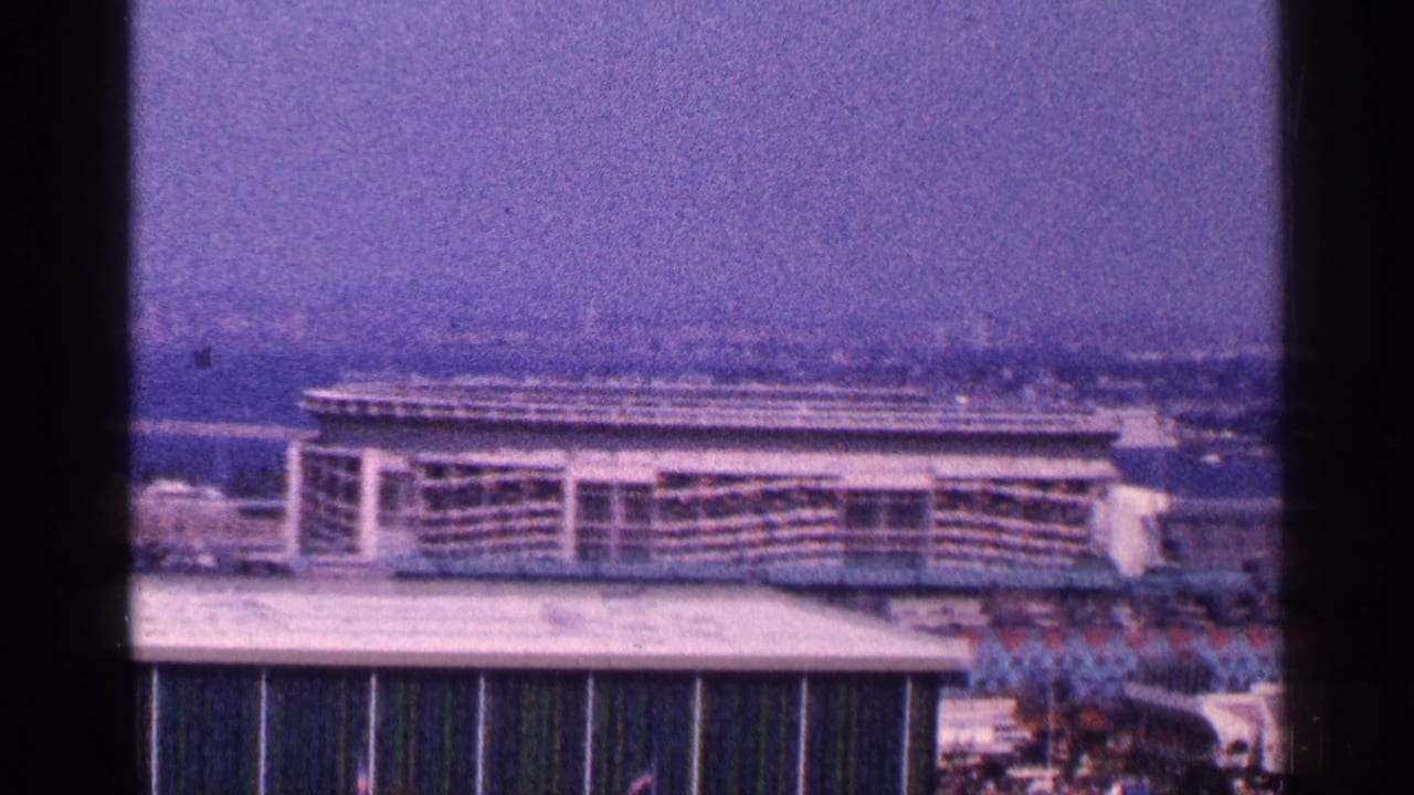 Elevated view of a fairground building with distant water and city structures beyond.