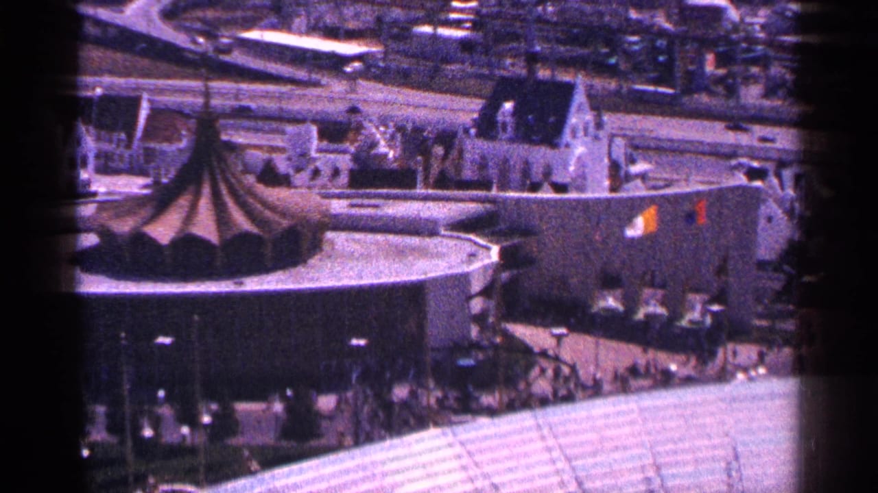 Elevated view of a round building with a conical roof beside city streets and rooftops.