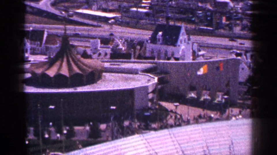 1964 New York City elevated view showing a round building with a conical roof, nearby streets, rooftops, and hazy background blocks.