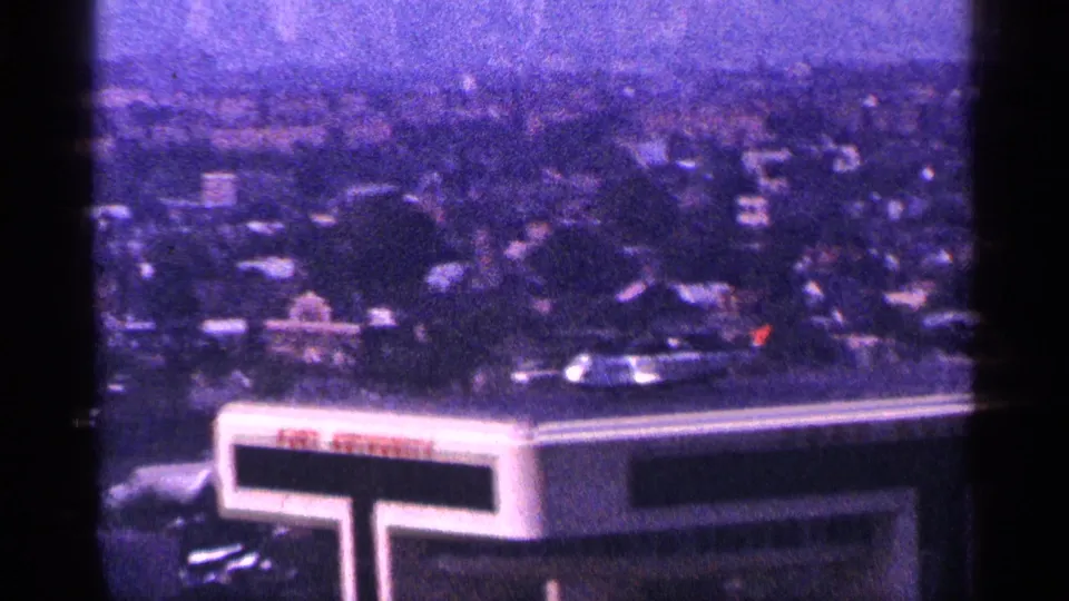1964 New York City elevated view looking past a rooftop marked Port Authority toward traffic, trees, and a hazy urban background.