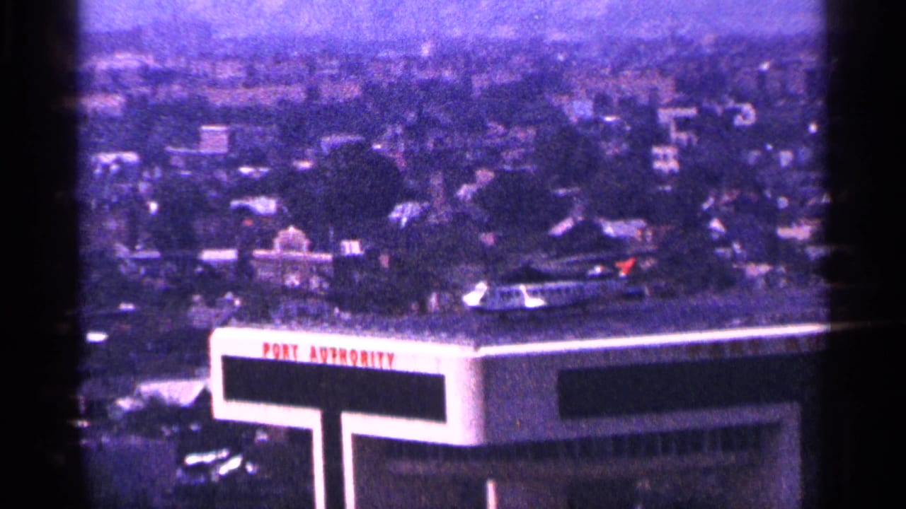 Rooftop helicopter near a Port Authority sign with hazy city skyline behind it.
