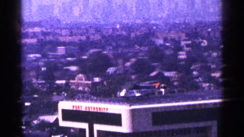1964 New York City frame of a rooftop helicopter above a clearly visible Port Authority sign and a soft, hazy urban background.