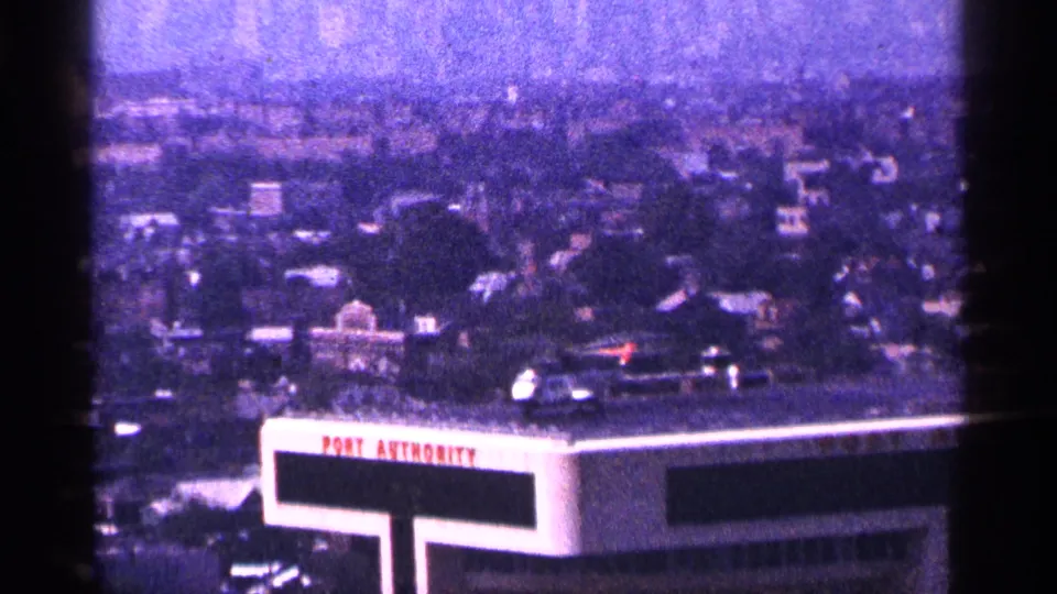 1964 New York City home-movie frame with a rooftop helicopter near the Port Authority sign and dense city blocks beyond.