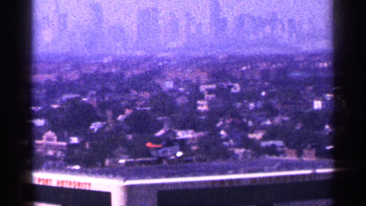 1964 New York City skyline seen from an elevated position, with dense rooftops and partial Port Authority lettering in front.