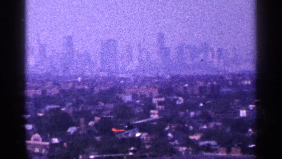 1964 New York City home-movie frame with a soft rooftop view and a distant skyline under purple-tinted haze.
