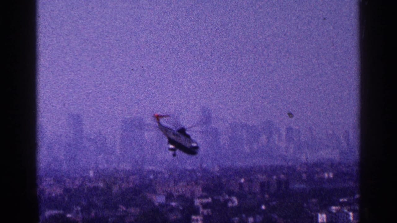 Helicopter flying over a hazy city skyline with purple-tinted film color.