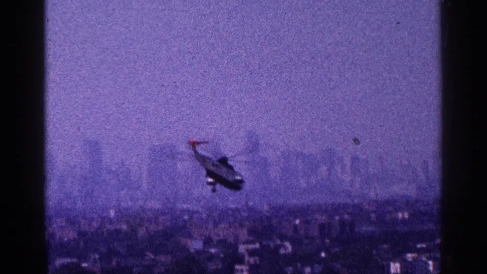 1964 New York City home-movie frame showing a helicopter above a distant, hazy skyline with strong grain and purple color shift.
