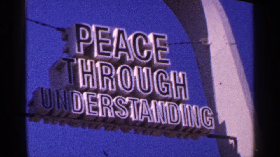 1964 New York City frame showing a blue public sign with white letters reading PEACE THROUGH UNDERSTANDING.