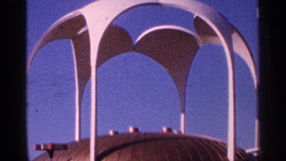 1964 New York City 8mm frame showing a distinctive white arched structure above a rounded roofline against clear blue sky.