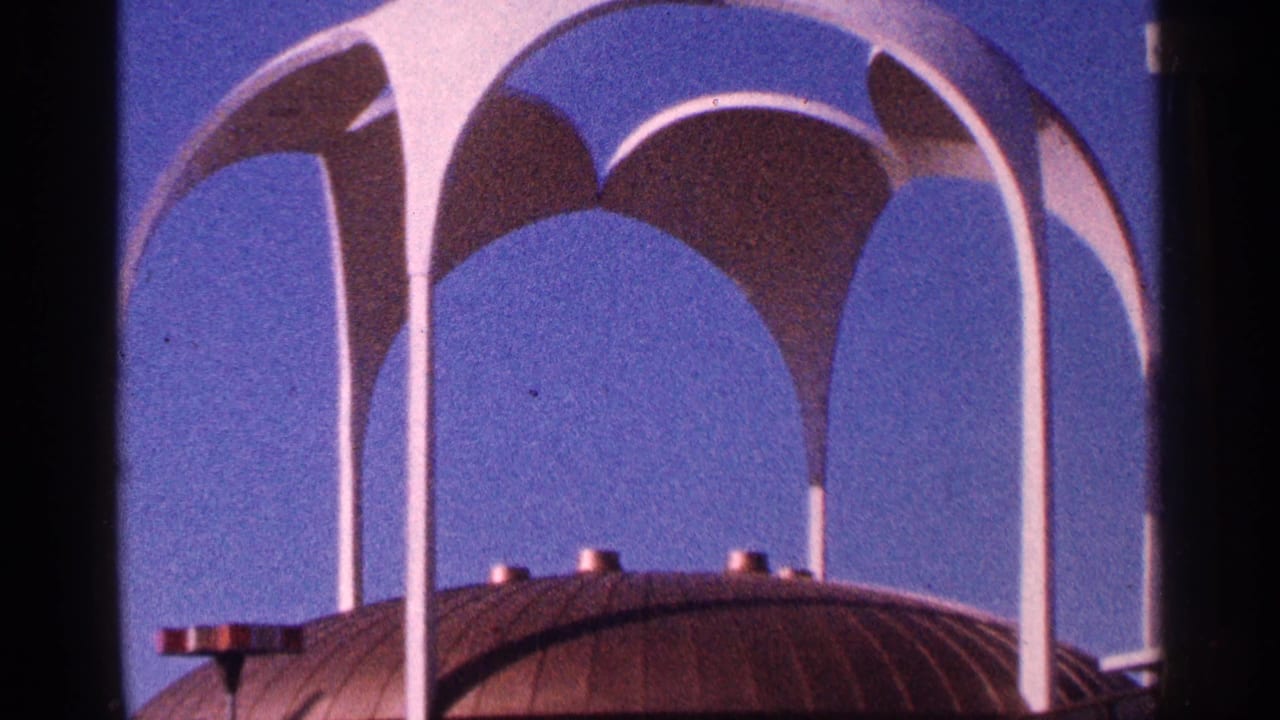 White arched architectural structure above a dark domed roof against blue sky.