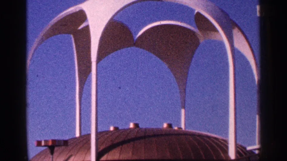 1964 New York City 8mm frame showing white arched mid-century forms over a dark domed roof under blue sky.