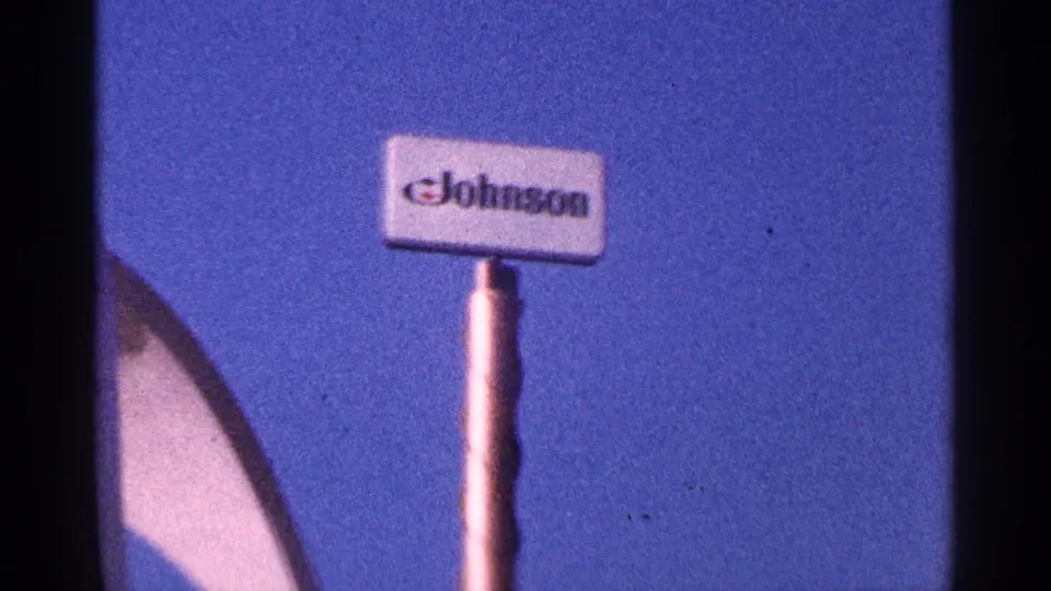 1964 New York City 8mm frame showing a Johnson sign near the white arched landmark structure under blue sky.