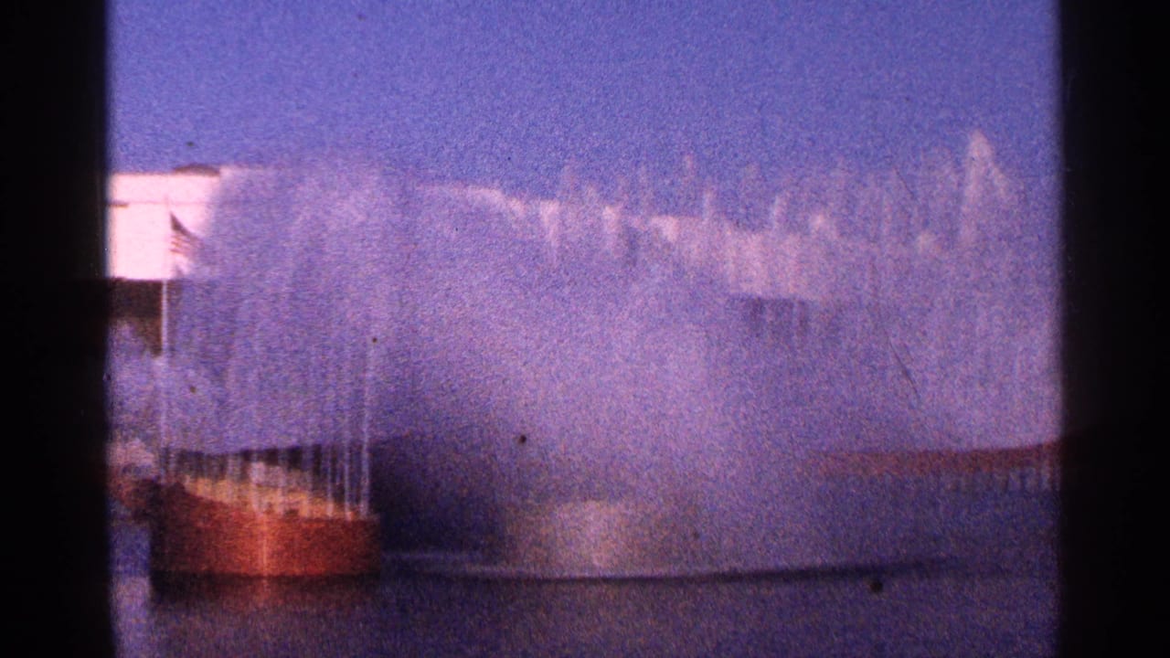 Fountain jets rise behind a low bridge-like structure under a purple-blue sky.