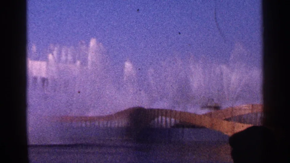 1964 New York City frame showing the fountain display behind a low structure and a partial foreground figure at lower right.