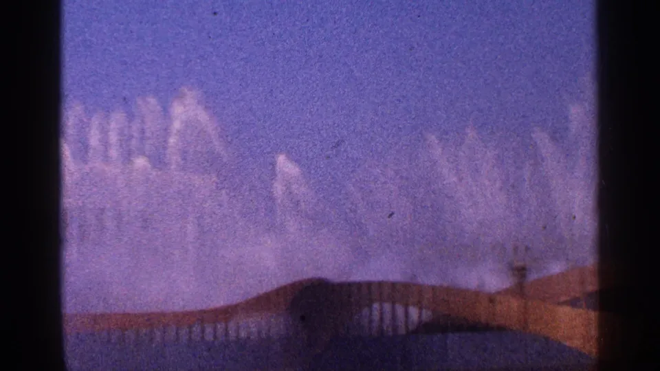 1964 New York City 8mm frame with white water plumes against blue sky and a curved structure crossing the lower frame.
