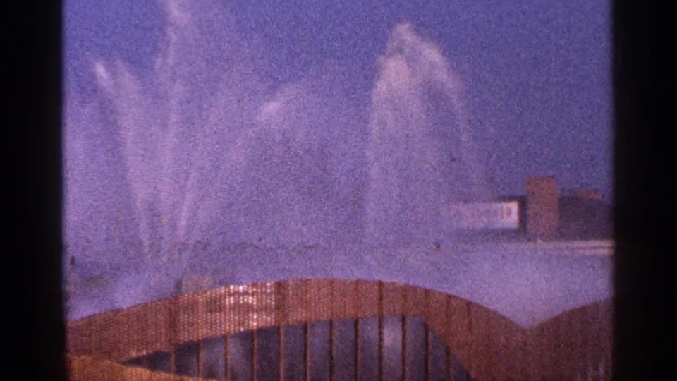 1964 New York City 8mm frame showing a broad burst of fountain spray behind a curved foreground railing or bridge form.