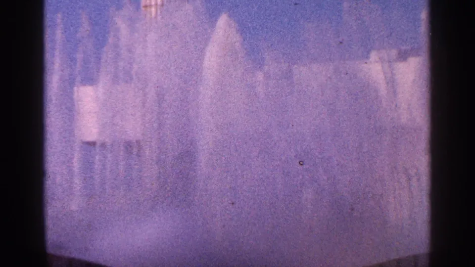 A soft 1964 New York City 8mm view of fountain spray and mist, with water plumes crossing a pale blue background.