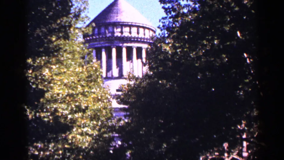 A white columned tower in New York City appears through leafy trees in a 1964 8mm home-movie frame.