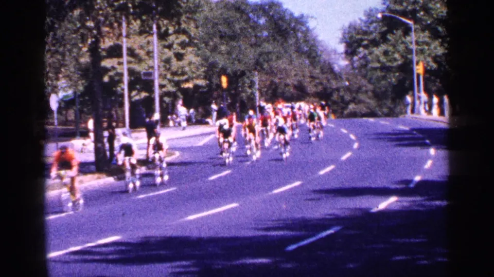 Several cyclists pass near the camera as the main 1964 New York City cycling group follows around the tree-lined curve.