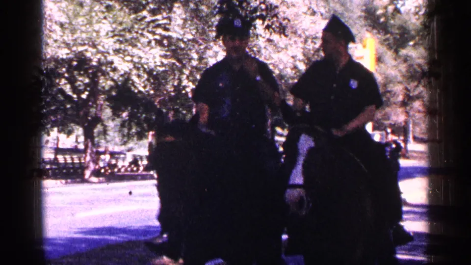 Two mounted police officers on horseback patrol a shaded New York City park area in this 1964 8mm home-movie frame.