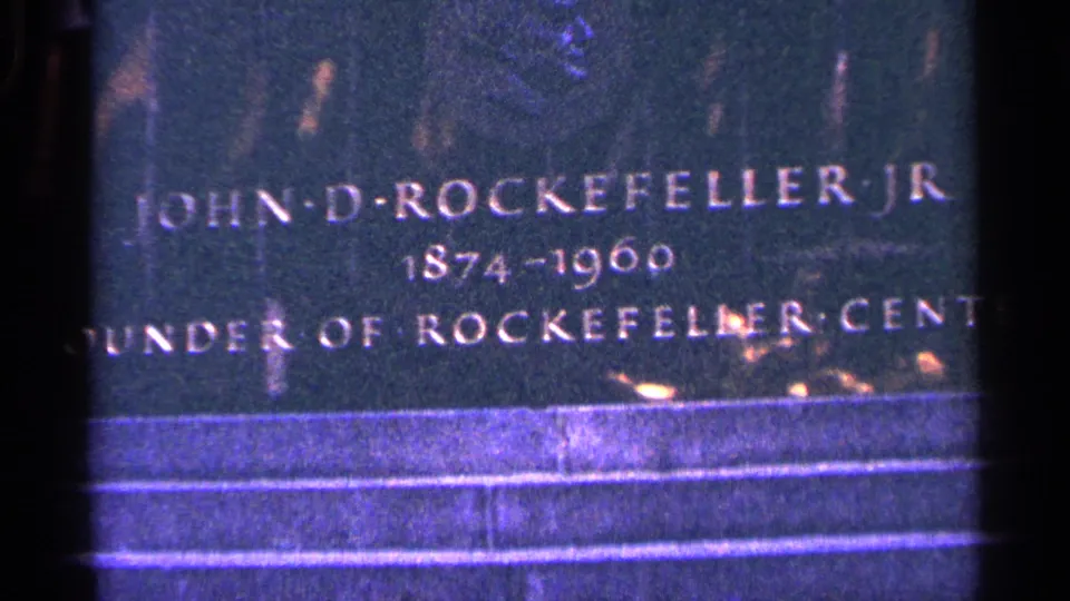Close-up of the John D. Rockefeller Jr. memorial plaque, with lettering and stone steps visible in vintage 8mm color.