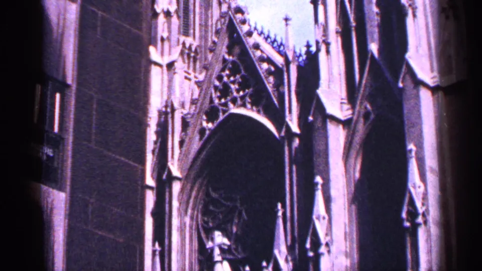 1964 New York City 8mm frame showing a Gothic-style church facade with pointed arch, stone tracery, and purple-tinted exposure.