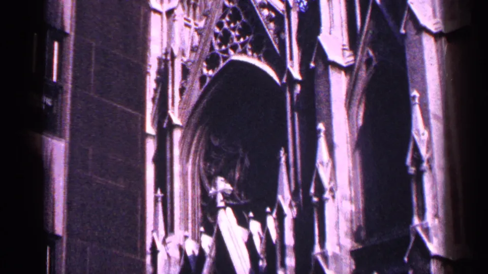 1964 New York City 8mm frame showing Gothic church architectural details, including a pointed entrance arch and ornamental stone elements.
