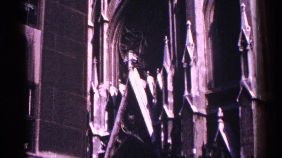 1964 New York City 8mm frame of a Gothic-style cathedral facade with vertical stone details and deep shadows.