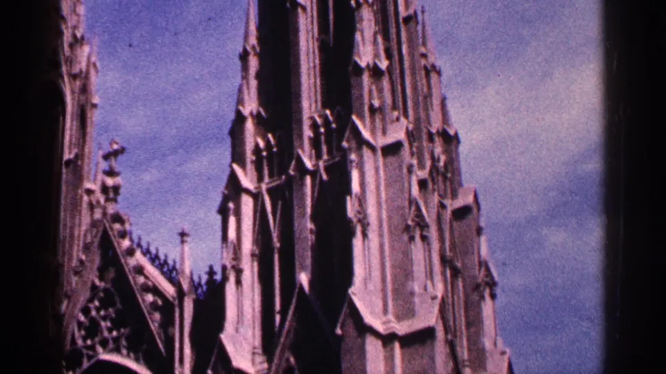 1964 New York City 8mm frame showing a cathedral spire, roofline finials, and dark arched architectural detail.