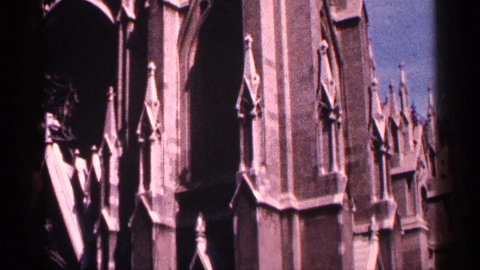 1964 New York City 8mm frame with tall Gothic arches, carved stone panels, and vertical spire-like details on a church exterior.