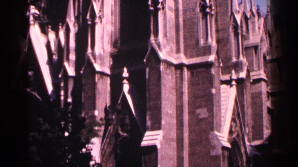 1964 New York City 8mm frame showing a shadowed portion of the Gothic church facade with pointed stone ornament and foliage near the base.