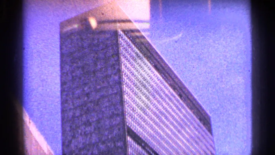 1964 New York City frame showing a low-angle view of a modern skyscraper with gridded windows under blue sky.