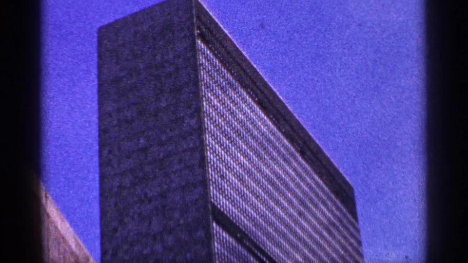 1964 New York City home-movie frame showing a tall modern building filmed from below against a deep blue sky.