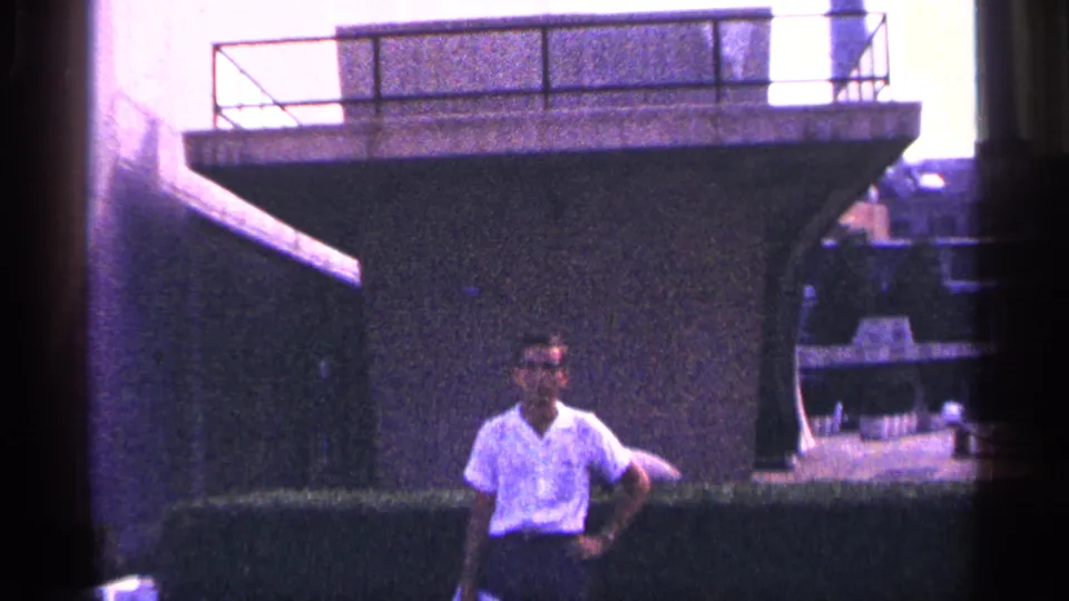 Adult man poses outdoors in New York City before a large concrete architectural feature, with 8mm grain and dark frame edges.