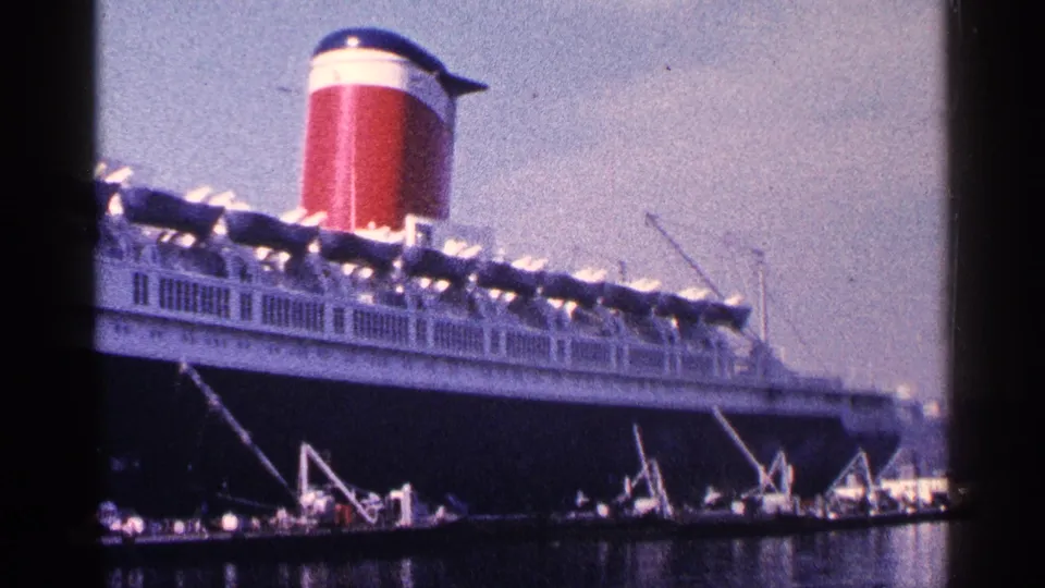 A large ocean liner appears docked in New York City harbor, with white upper decks, a red funnel, and port machinery near the waterline.