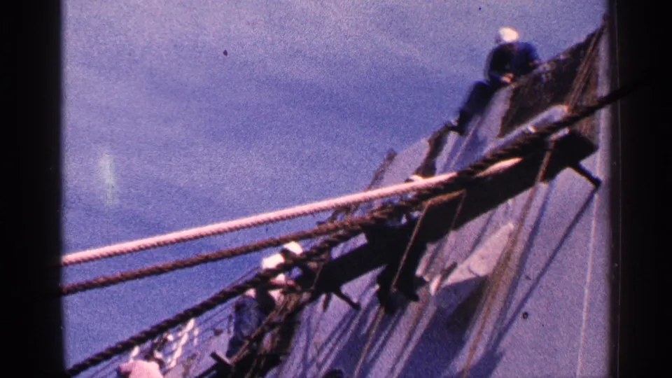 Crew members appear on the rigging beside the Queen Mary hull in 1964 New York City harbor footage.
