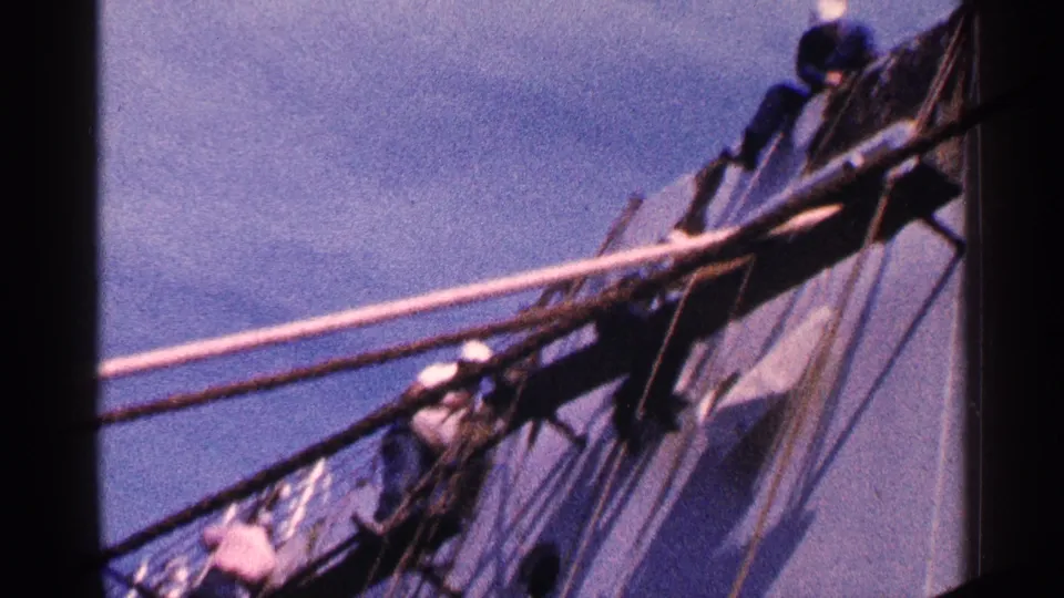 A handheld 8mm view angles up toward workers and rope lines along a docked ship in New York City.