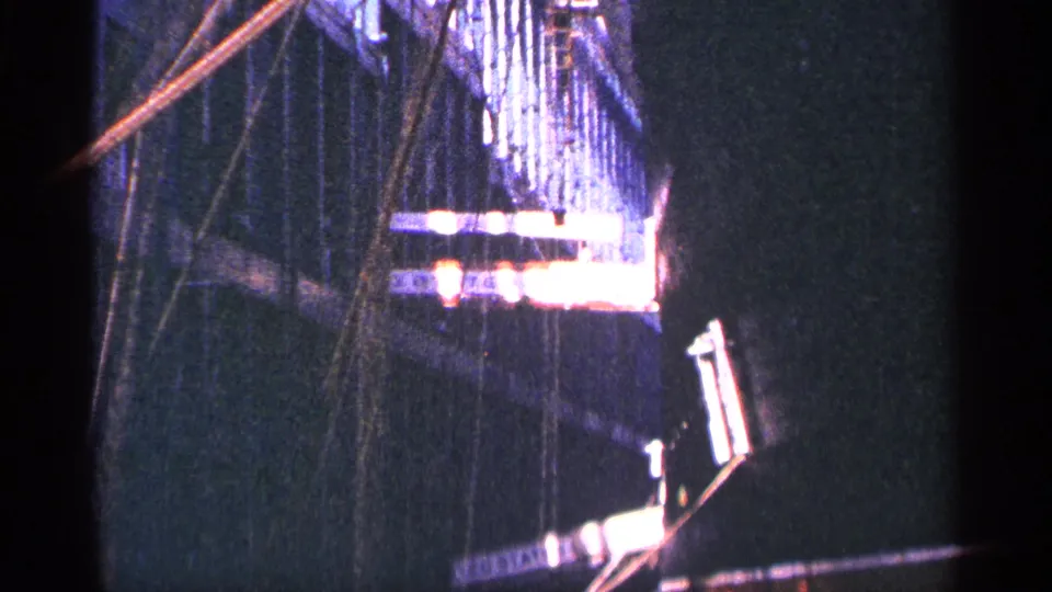 Handheld 8mm frame from the clip opening, showing a dark partial view before the Children's Garden sign becomes clear.
