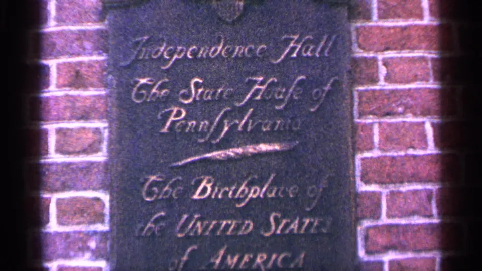 Handheld 8mm view of the Independence Hall plaque, with soft focus and magenta-shifted color across the brickwork.