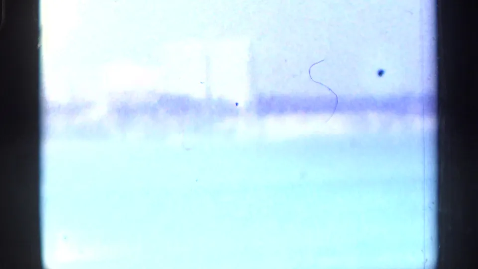 Bright, washed 8mm frame with a faint horizon line, indistinct distant forms, scratches, and dark film edges.