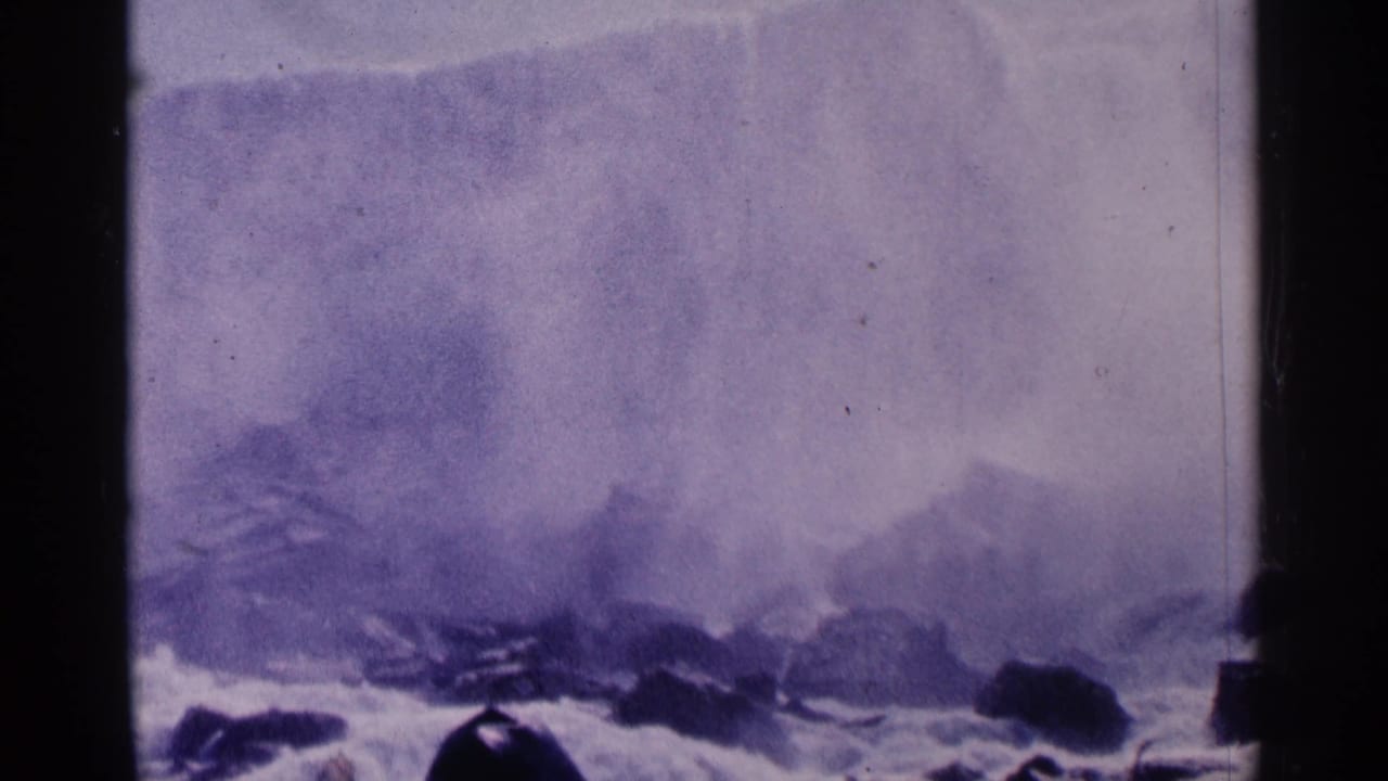 Mist rises over rocks beside a broad waterfall.