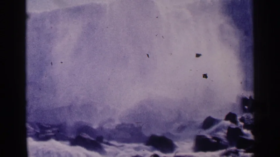 1964 Niagara Falls home-movie frame with heavy spray, rocky foreground and a small visitor near the lower edge.