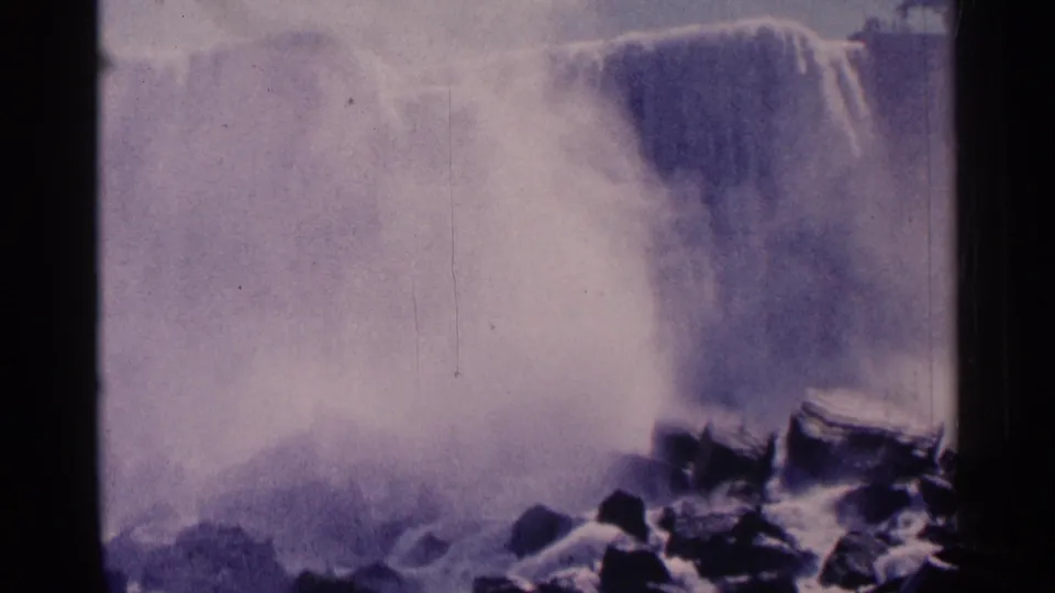 Purple-tinted 8mm view of Niagara Falls with a small visitor near rocks below the falling water.
