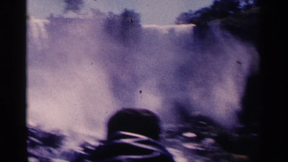 1964 8mm home-movie view of Niagara Falls mist and water with a dark silhouetted observer shape in the foreground.