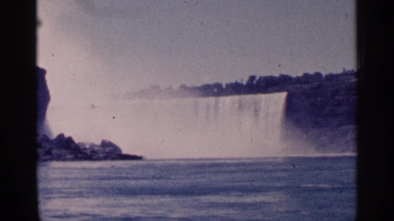 Wide waterfall view across river water with mist and distant tree line.